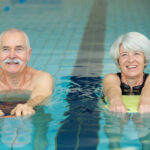 Ein älteres Ehepaar macht Schwimmübungen im Pool